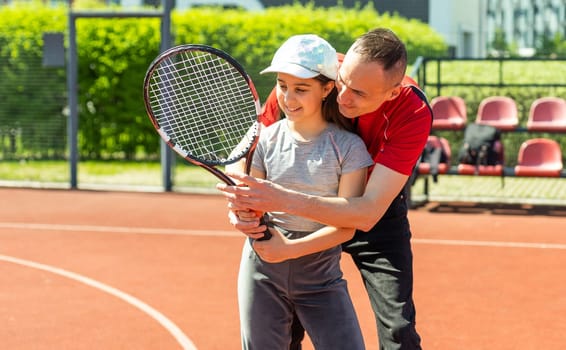 Father is a tennis coach for his daughter. Female child is playing in tandem with her daddy in doubles tennis.