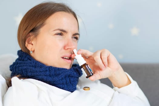 A young woman with bad cold lying in bed under the blanket and using nasal drops. Woman using nose spray.