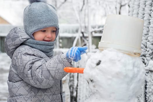 Cute little boy is making a snowman. Child playing with snow. Children wintertime outdoor activitie time concept.