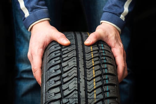 Closeup of mechanic hands holding a tire on dark background. Replacement of winter and summer tires.