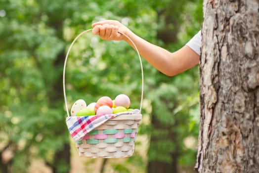 Child hand holding basket full of colorful easter eggs after egg hunt at spring time. Happy Easter day.