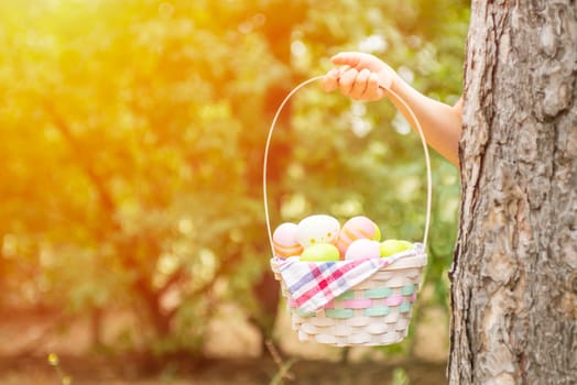 Childrens hand holding basket with colorful easter eggs in garden or park. Happy Easter background. Copy space for text.