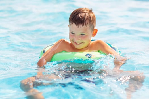 Funny happy child boy in swimming pool on inflatable rubber circle ring. Kid playing in pool. Summer holidays and vacation concept.