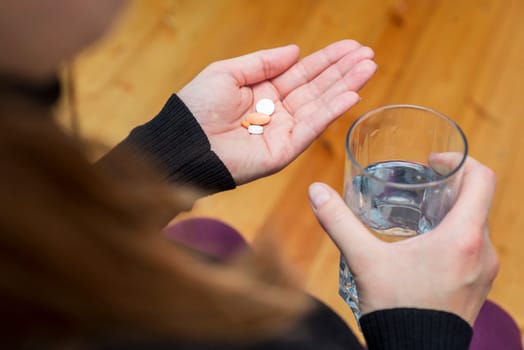 Woman holds tablet and glass of water. Female going to take tablet from headache or painkiller or abortion pill medication drinking clear water from glass.