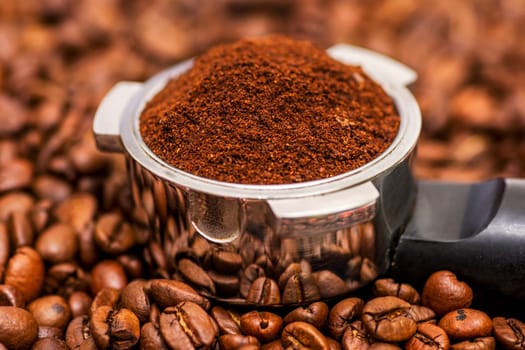 Freshly ground coffee in a metal filter on background coffee beans. Espresso filter holder for coffee machine with ground coffee.