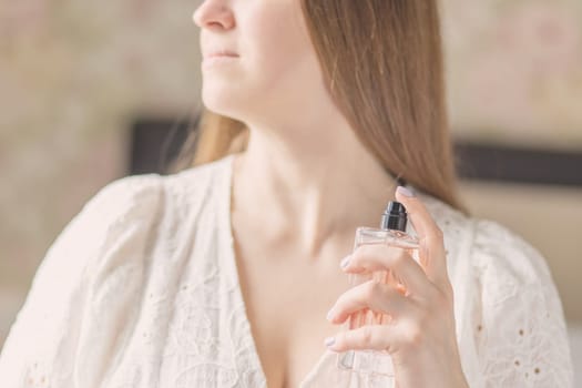 Beautiful young woman with bottle of perfume at home, closeup.
