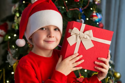 Child near Christmas tree with gift box. Cute little boy is standing near Christmas tree with gift. Merry Christmas and Happy New Year.