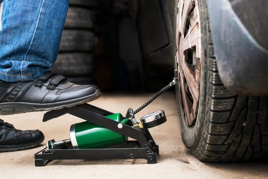 Man's foot pumping up a flat car tyre or tire, which is deflated. Man Inflating car tyre with foot pump. Concept of checking a car before traveling .