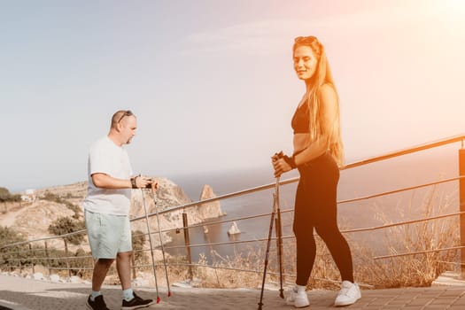 Happy Middle aged couple or friends practicing nordic walking in park near sea. Mature couple with trekking poles walking, practicing Nordic walking outdoors. Aging youthfully and sport concept.