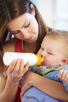 Mother, baby and holding with bottle in home of formula, feeding or hunger for future growth. Woman, infant or son with nutrition for child development, milestone and health in kitchen with bonding.