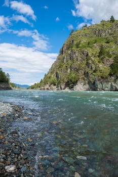 A wide, full-flowing mountain river with a fast current. Large stones stick out of the water. The large turquoise-colored mountain river Katun in the Altai Mountains, Altai Republic.