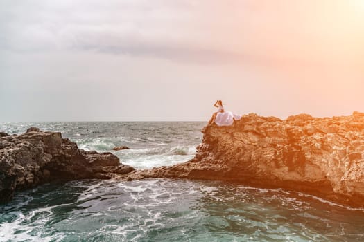 Woman sea white dress. A woman in a storm sits on a stone in the sea. Dressed in a white long dress, waves crash against the rocks and white spray rises