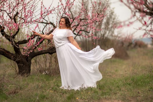 Woman peach blossom. Happy woman in white dress walking in the garden of blossoming peach trees in spring.