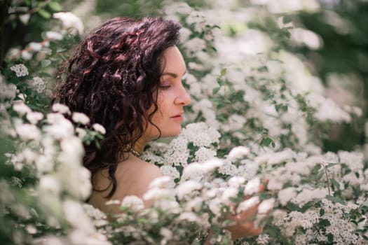 Woman spirea flowers. Portrait of a curly happy woman in a flowering bush with white spirea flowers