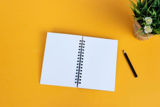Directly above view of office desk with pen, notepad, and potted plant on yellow background. Copy space. Flat lay.