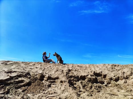 Dog German Shepherd and woman on large sandy mountain or dune in nature in summer, spring, autumn day. Russian eastern European dog veo and the mistress, trainer outside and outdoors during training