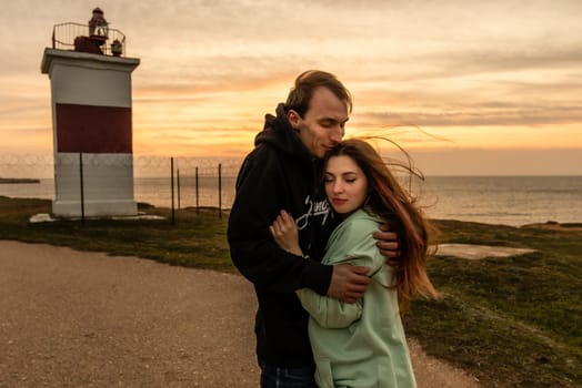 Portraits of lovers, romantic couple of lovers hugging, kissing, touching, eye contact at sunset, sunrise against the background of the sea, sun, clouds in fiery red, orange colors.