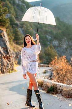 woman umbrella leaves , She holds him over her head, autumn leaves are falling out of him. Beautiful woman in a dress with an umbrella in the autumn park on the road in the mountains