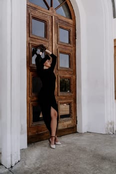 Stylish woman in the city. Fashion photo of a beautiful model in an elegant black dress posing against the backdrop of a building on a city street.