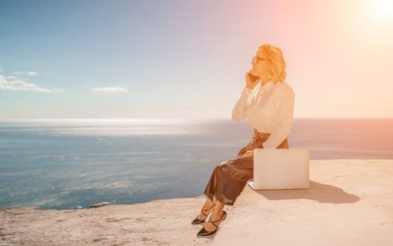 Business woman on nature in white shirt and black skirt. She works with an iPad in the open air with a beautiful view of the sea. The concept of remote work