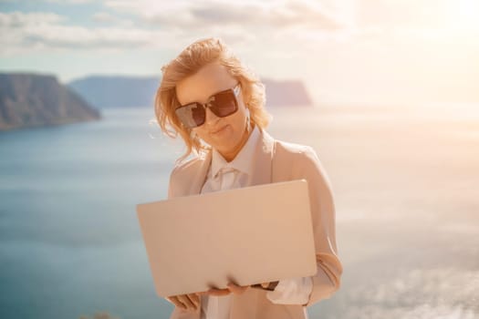 Freelance women sea. She is working on the computer. Good looking middle aged woman typing on a laptop keyboard outdoors with a beautiful sea view. The concept of remote work