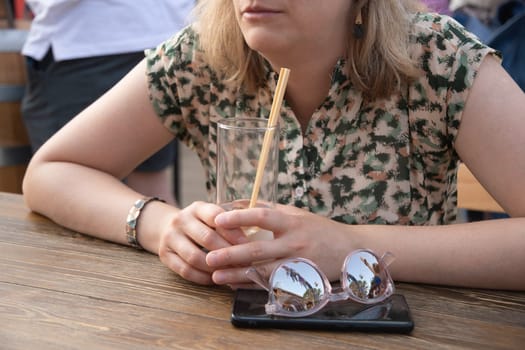 unrecognizable young woman holding glass with cold exotic cocktail, sitting at table in street cafe on sunny gold time, woman drinking cool lemonade, High quality photo