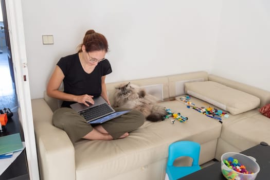 A woman sitting on a couch with a cat and a laptop
