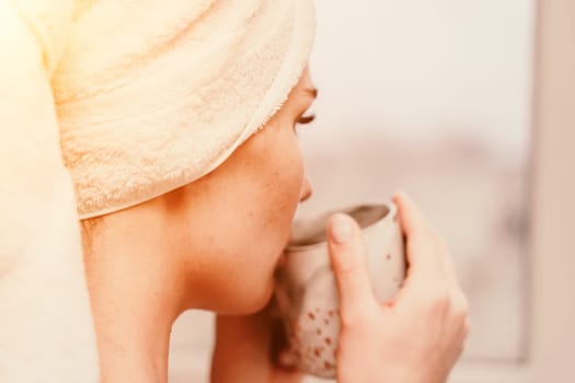 Young serene relaxed woman in spa bath towel drinking hot beverage tea coffee after taking shower bath at home. Beauty treatment, hydration concept