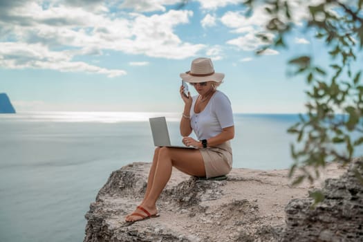 Freelance women sea working on the computer. Good looking middle aged woman typing on a laptop keyboard outdoors with a beautiful sea view. The concept of remote work