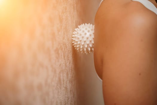 Athletic slim caucasian woman doing thigh self-massage with a massage ball indoors. Self-isolating massage.