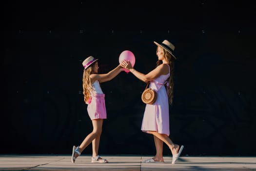 mother and daughter stand in pink dresses with flowing long hair on a black background. Enjoy communicating with each other.
