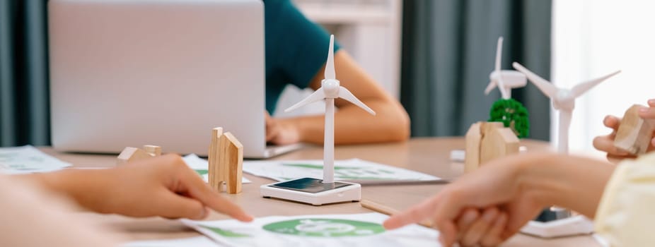 Windmill model represented using renewable energy placed during presenting green business on table with wooden block and environmental document scatter around. Closeup. Delineation.