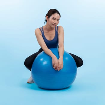 Young attractive asian woman portrait in sportswear with fit ball targeting on abs muscle for effective energetic daily workout routine. Studio shot and isolated background. Vigorous