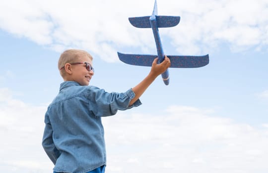 Happy child playing with a toy airplane against a blue sky in an open field.