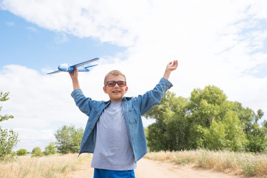 Happy child playing with a toy airplane against a blue sky in an open field.