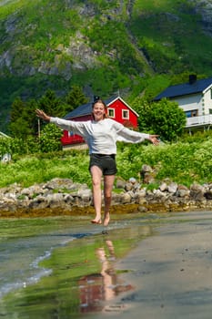 Young girl teenager running on beach in Norway Fjord. Vacation in Nordland in summer.