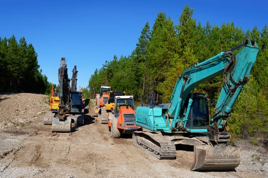 Heavy Construction Equipment, Tractors, Excavators, and Bulldozers Parked in a Forest Parking Lot. New Communication Line Installation