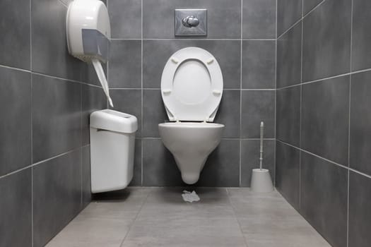 White toilet and trash can in a gray restroom - toilet paper on the floor. Mid shot