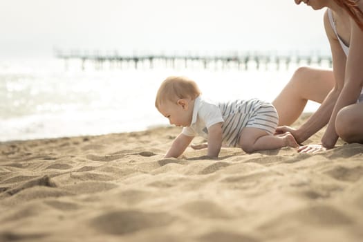 A little baby boy crawling on a sand on the seaside. Mid shot