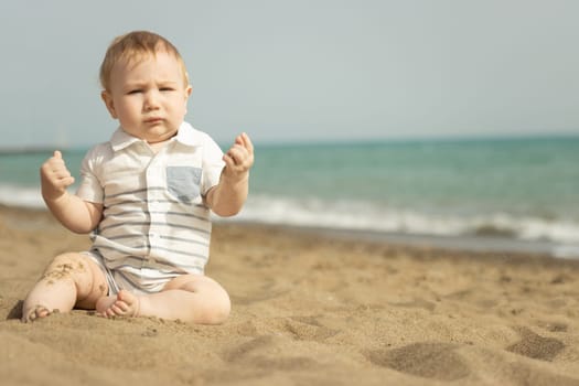 A baby boy sitting on a sand on the seaside. Mid shot