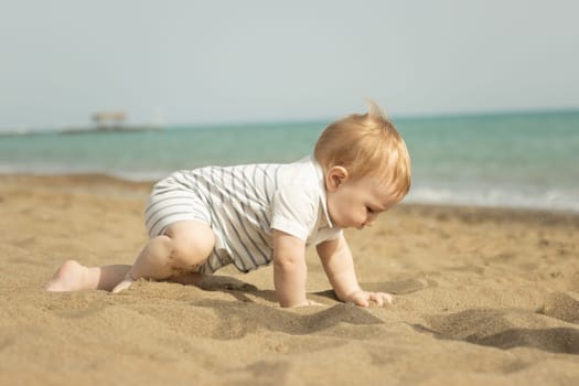 A baby boy crawling on a sand on the seaside. Mid shot