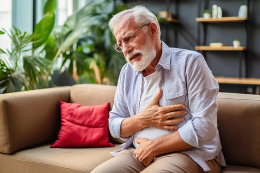 An elderly man sits on the sofa holding his chest, suffering from pain in his heart. High quality photo