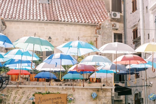 Colorful umbrellas hang on ropes above the street near an ancient stone house. High quality photo