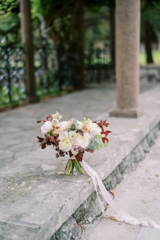Wedding bouquet of flowers stands on a stone border near a column in the garden. High quality photo