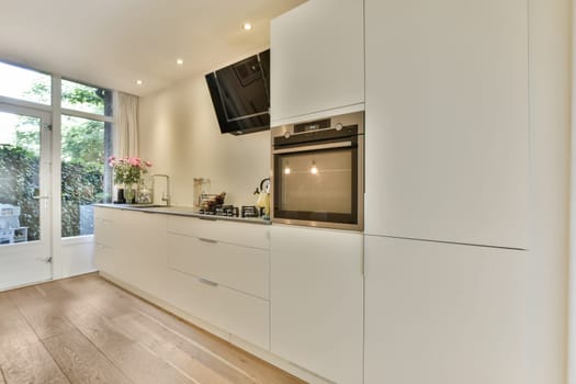 a kitchen with wood flooring and white cabinets in the center of the image is an open door leading to a patio