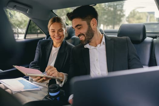 Cheerful business people have online meeting using laptop while sitting in car back seats