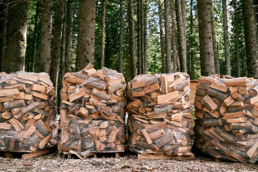 Stacks of firewood in mesh bags stand on pallets in the forest. High quality photo