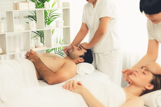 Caucasian couple enjoying relaxing anti-stress head massage and pampering facial beauty skin recreation leisure in dayspa modern light ambient at luxury resort or hotel spa salon. Quiescent