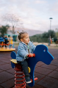Little girl sits on a swing-spring holding the handles and looks ahead. High quality photo