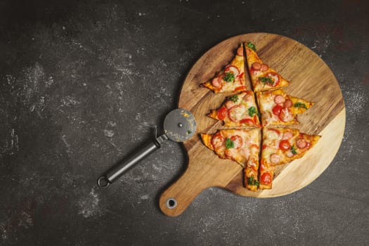 Cut Christmas tree pizza on a cutting board with a scabbard on the right against a dark background with copy space on the left, top view close-up.